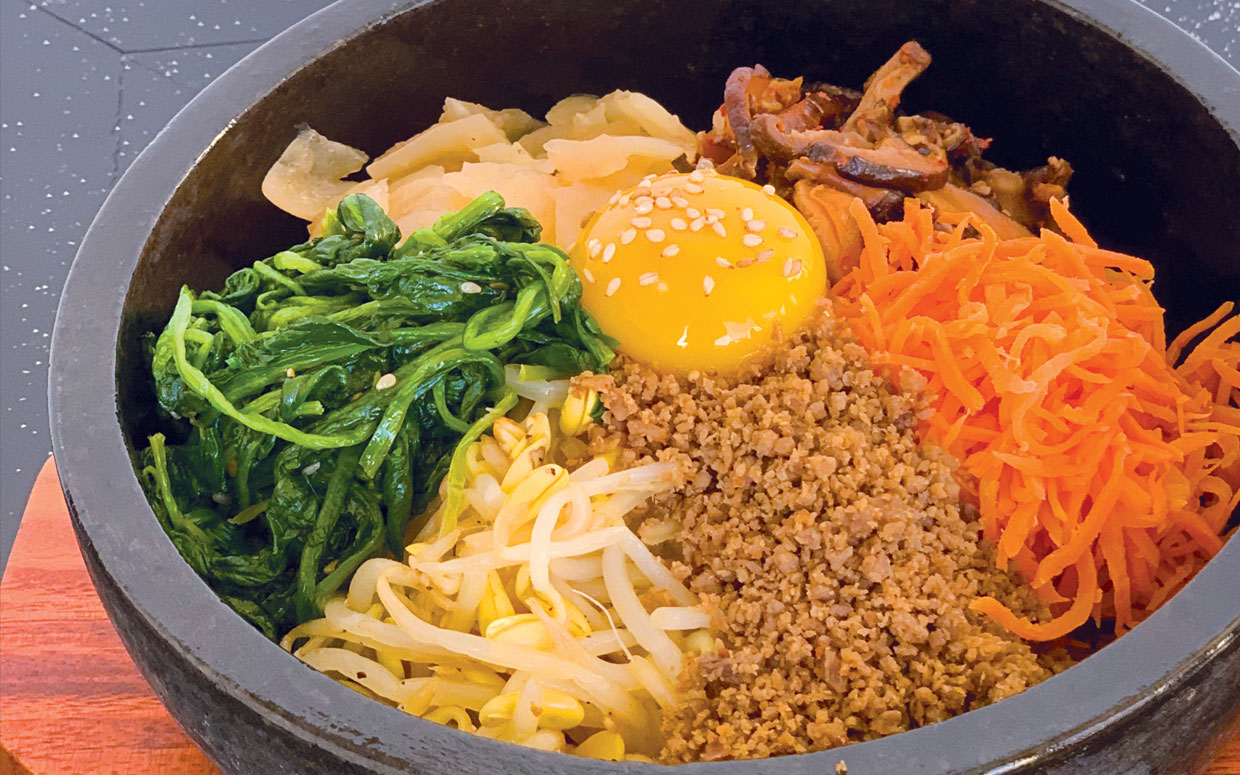 Ishiyaki Bibim Bap. Cooked seasoned vegetables, egg yolk and ground beef. served in a sizzling stone pot
